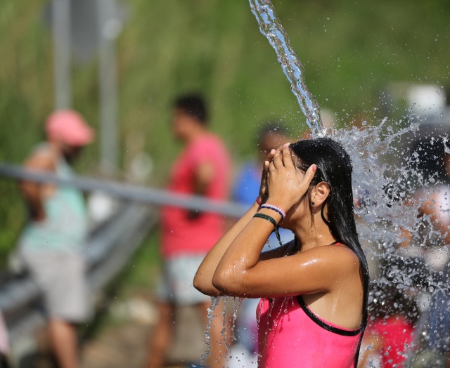 A young woman cools off under spring water from a mountain as people wait to fill containers Oct. 21 in Utuato, Puerto Rico. The town was without power or water for more than a month after Hurricane Maria devastated the island. (CNS/Bob Roller)